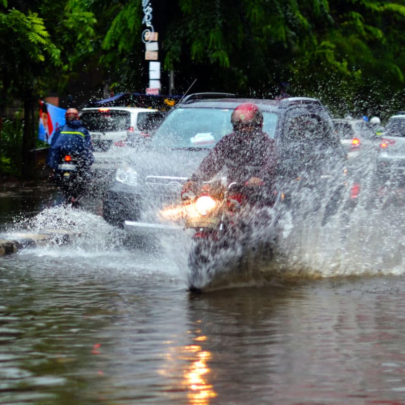 Scooter and car driving through flooding of the road after strong rain in Bali