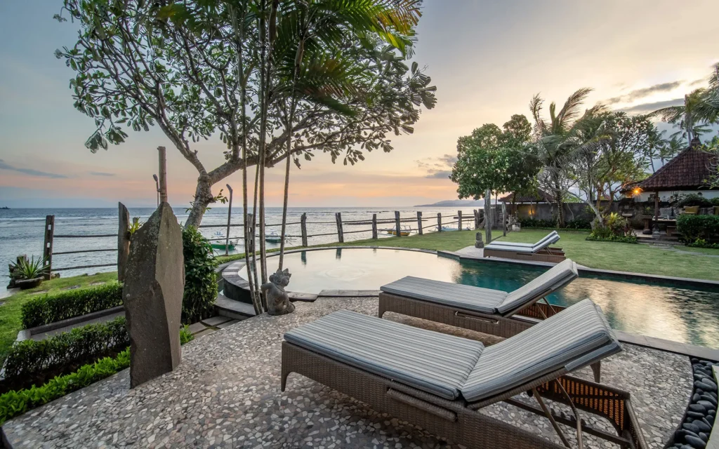 Sun loungers facing the ocean next to a private swimming pool during a peaceful sunset at Bali Hidden Villas.