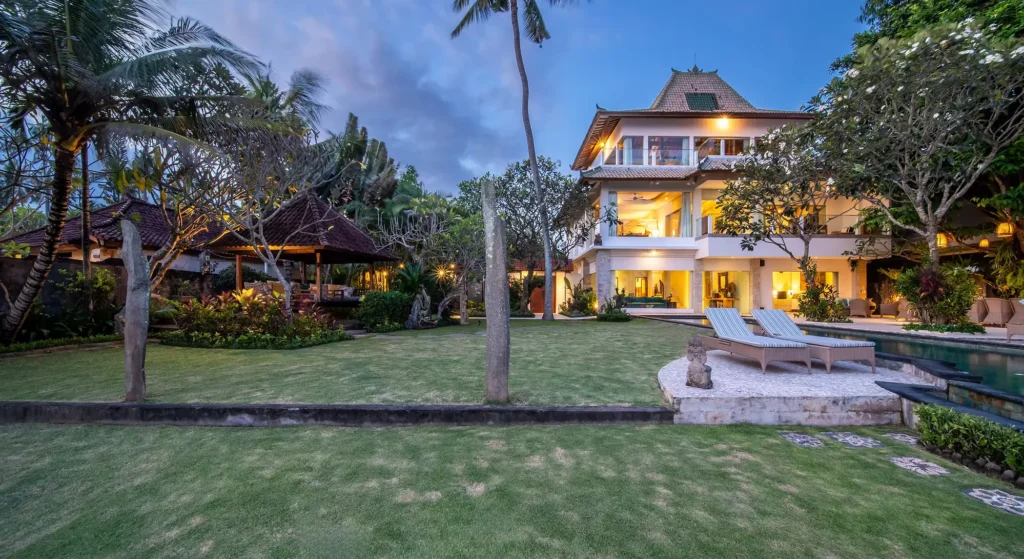 A wide-angle twilight view of the three-story Villa Cocoa Maya with a massive private lawn and swimming pool at Bali Hidden Villas, Ubud.