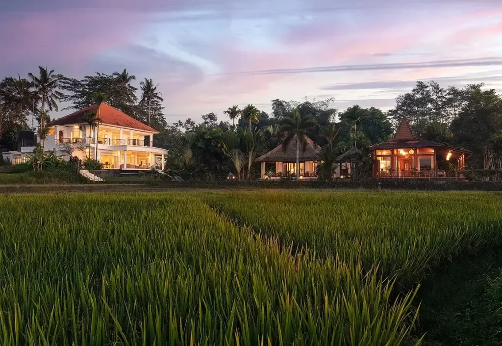 Panoramic twilight view of Villa Tau and traditional wooden pavilions overlooking lush green rice paddies at Bali Hidden Villas in Ubud.