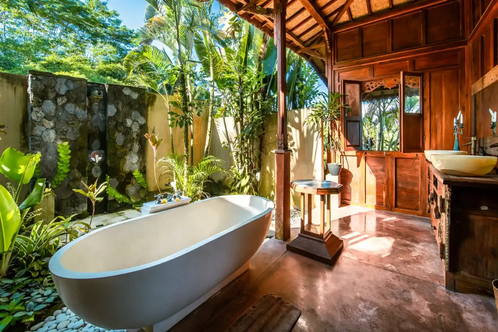 Luxury open-air bathroom in a private villa at Bali Hidden Villas, featuring freestanding tub, rustic stone wall, and tropical greenery in Ubud.