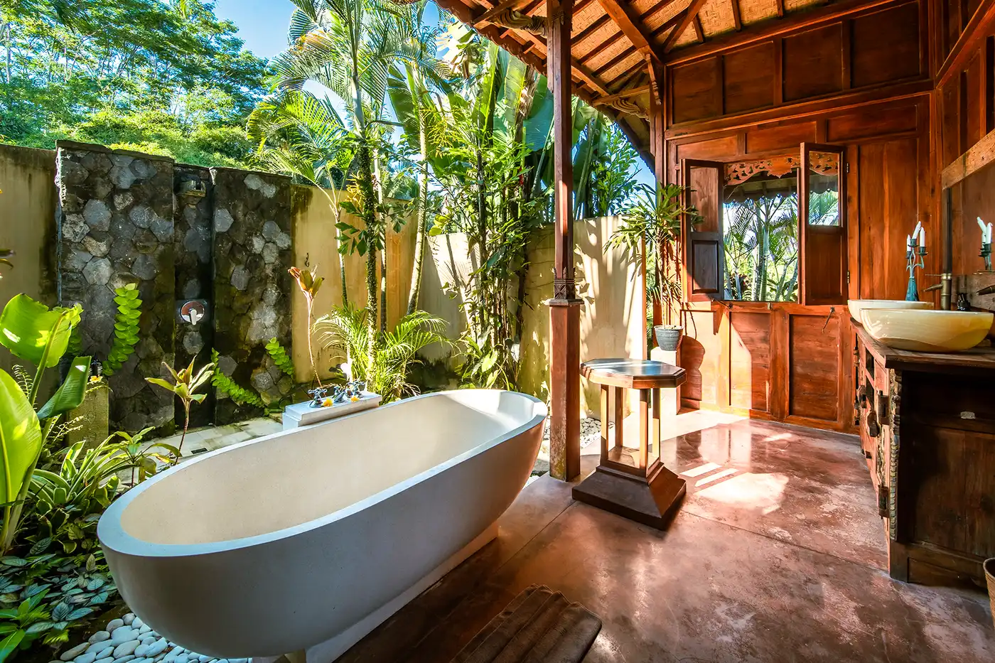 Luxury open-air bathroom in a private villa at Bali Hidden Villas, featuring freestanding tub, rustic stone wall, and tropical greenery in Ubud.