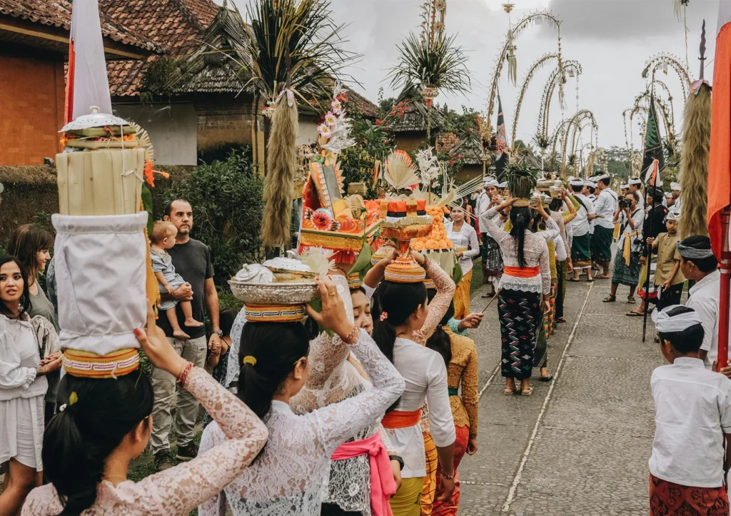 10 Most Important Ceremonies in Bali Balinese women carrying ceremonial offerings during a traditional village procession in Bali with decorated penjor lining the streets.